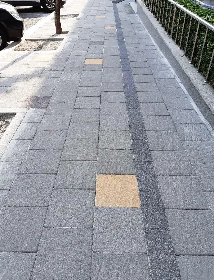 울산 낭만의거리 난간 옆 곧은 보도. 사암 결이 보이는 회색 판형 블록에 베이지 블록이 드문드문 섞이고 짙은 회색 띠가 한 줄로 이어진다.